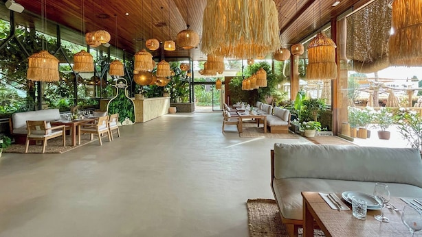 A spacious indoor area with wooden ceiling and hanging rattan chandeliers, furnished with tables and chairs, and large windows offering views of greenery outside. - Torre Melina, a Gran Meliá Hotel (Barcelona)