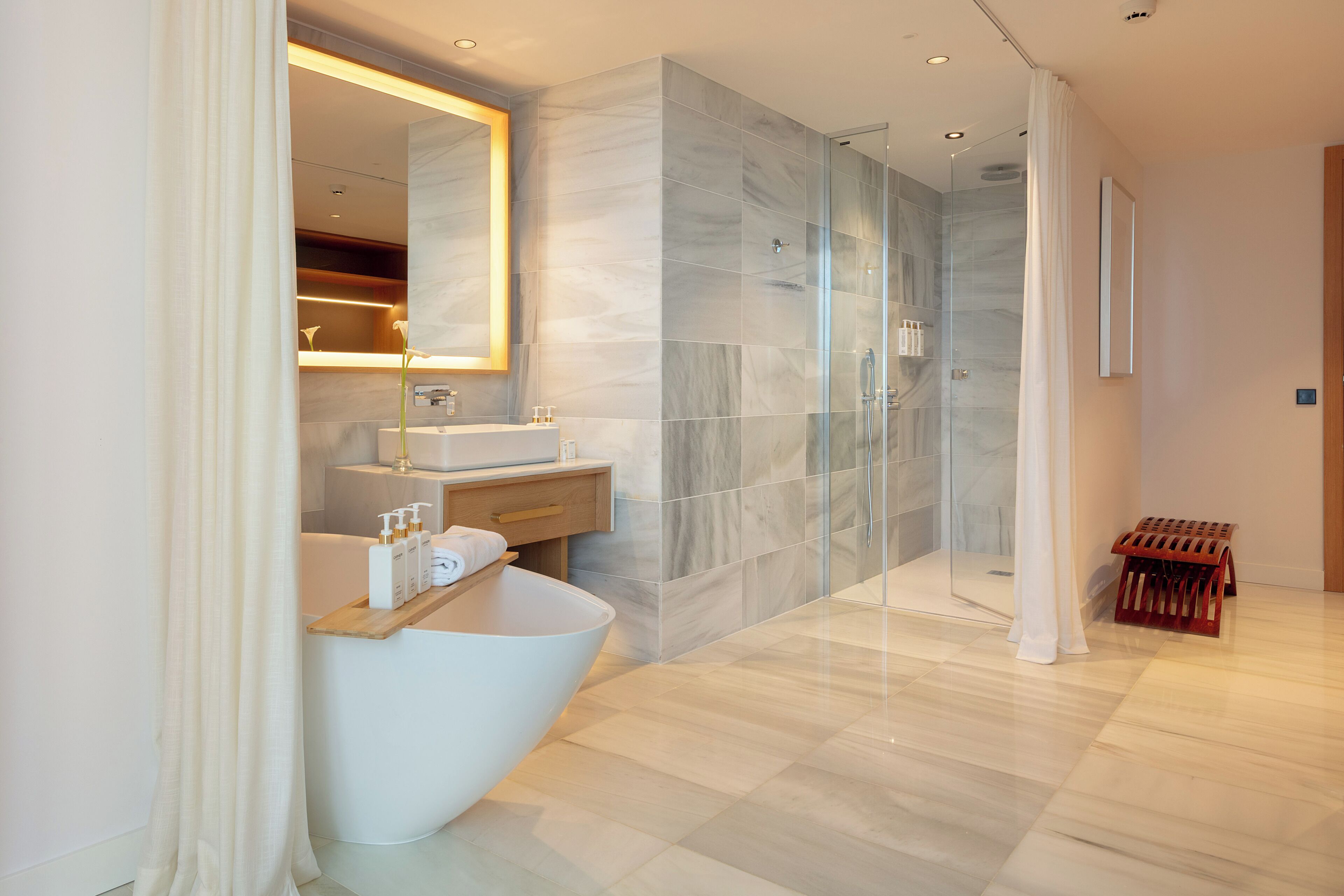 A modern bathroom with a freestanding bathtub, a glass-enclosed shower, and a marble-tiled wall.