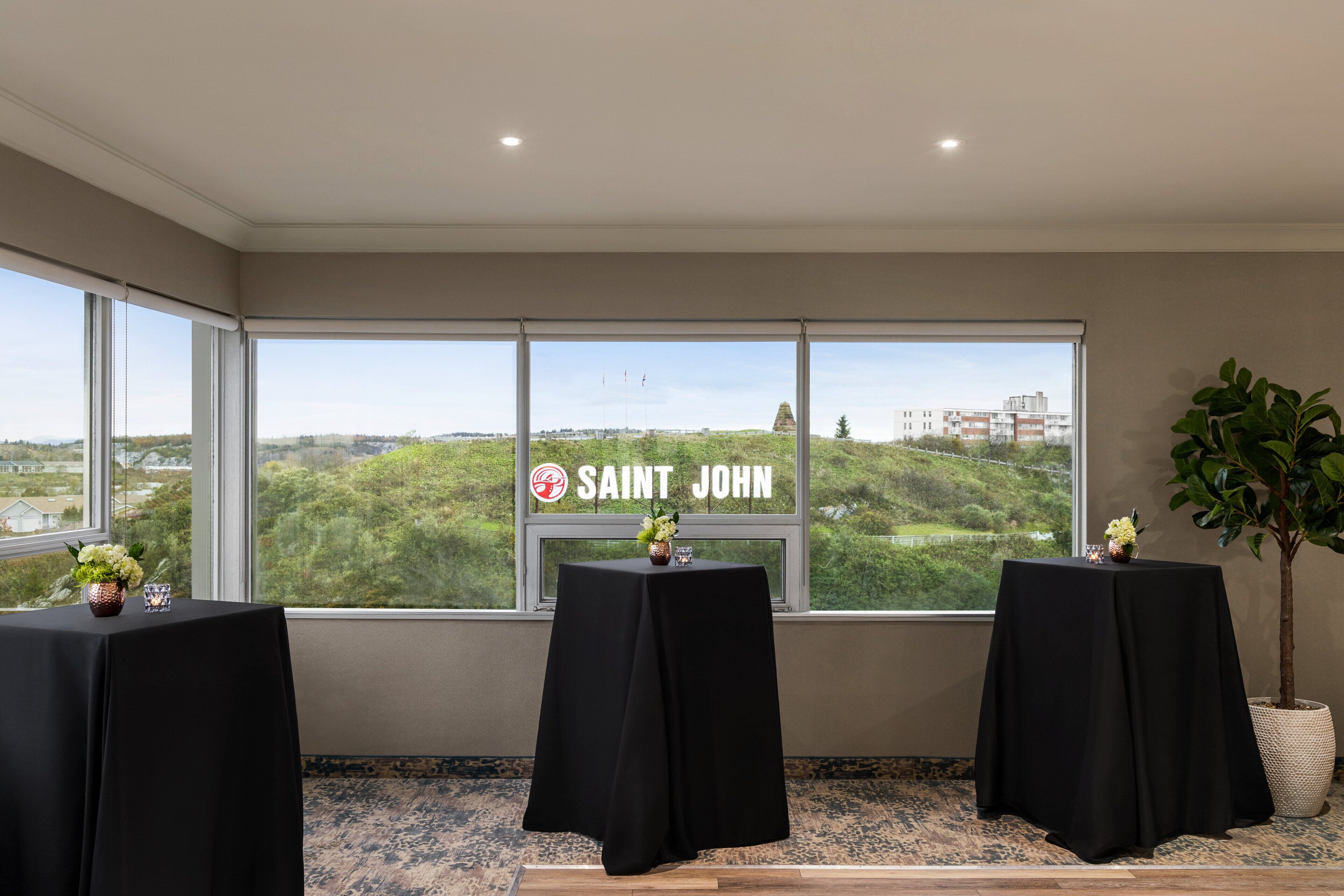A room with three tables covered in black tablecloths, a large window with a view of greenery and buildings, and a sign reading "SAINT JOHN".