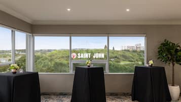 A room with three tables covered in black tablecloths, a large window with a view of greenery and buildings, and a sign reading "SAINT JOHN".