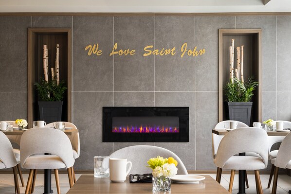 A modern dining area with a fireplace, two wooden sideboards, and a wall-mounted TV.