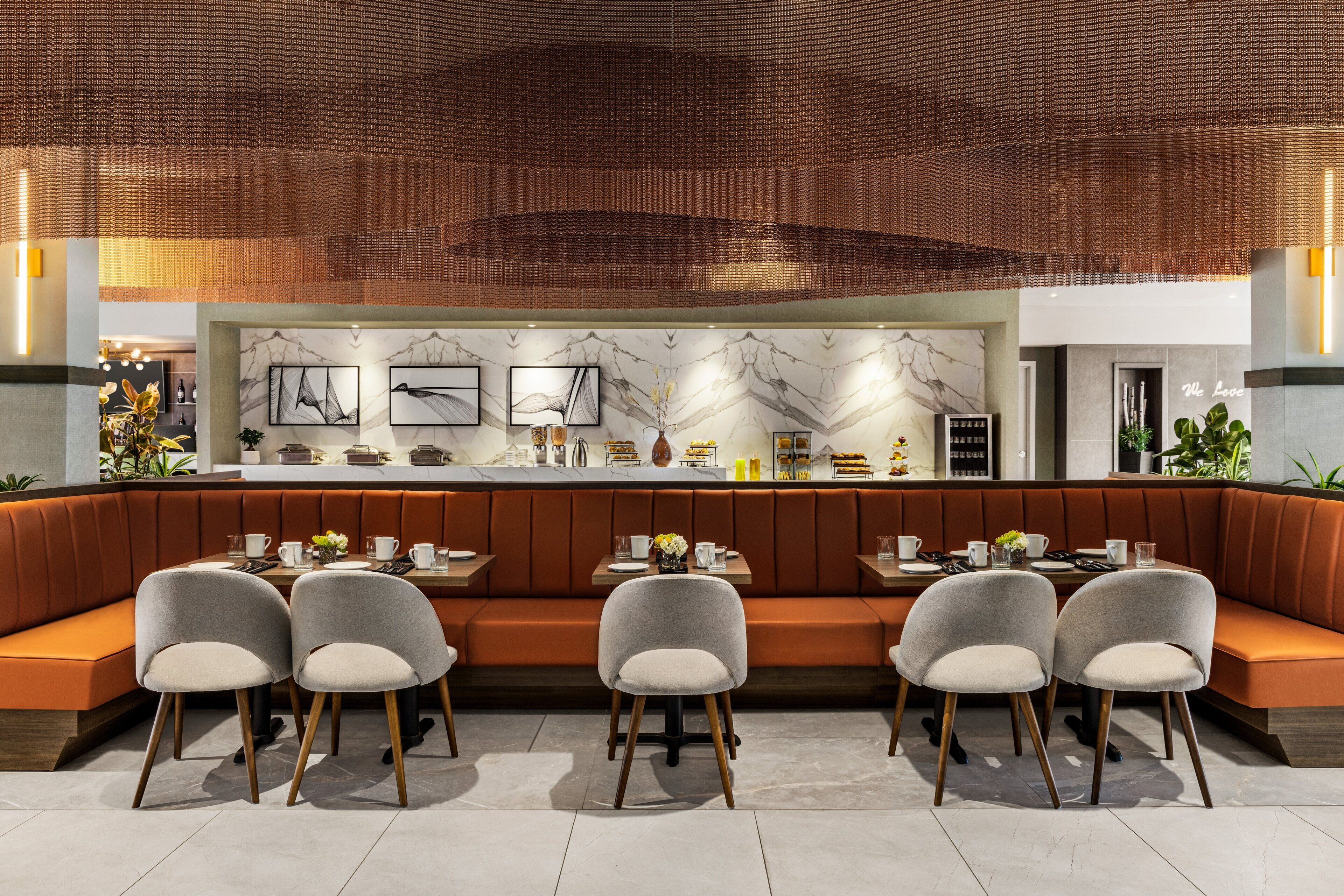 A modern restaurant with a long counter, cushioned seating, and marble wall decor.