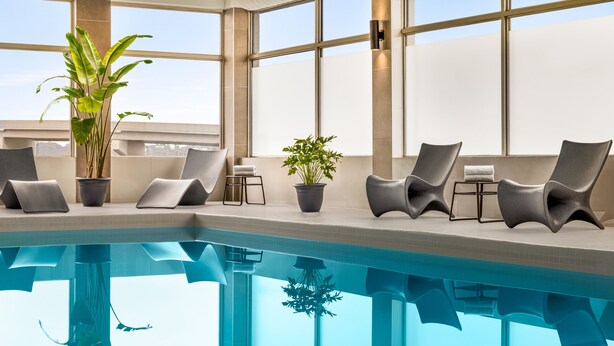 Un área de piscina interior moderna con sillones de descanso y plantas en macetas.