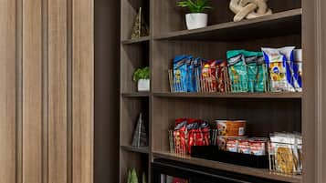 Una despensa con estantes llenos de aperitivos, una planta en maceta y objetos decorativos.