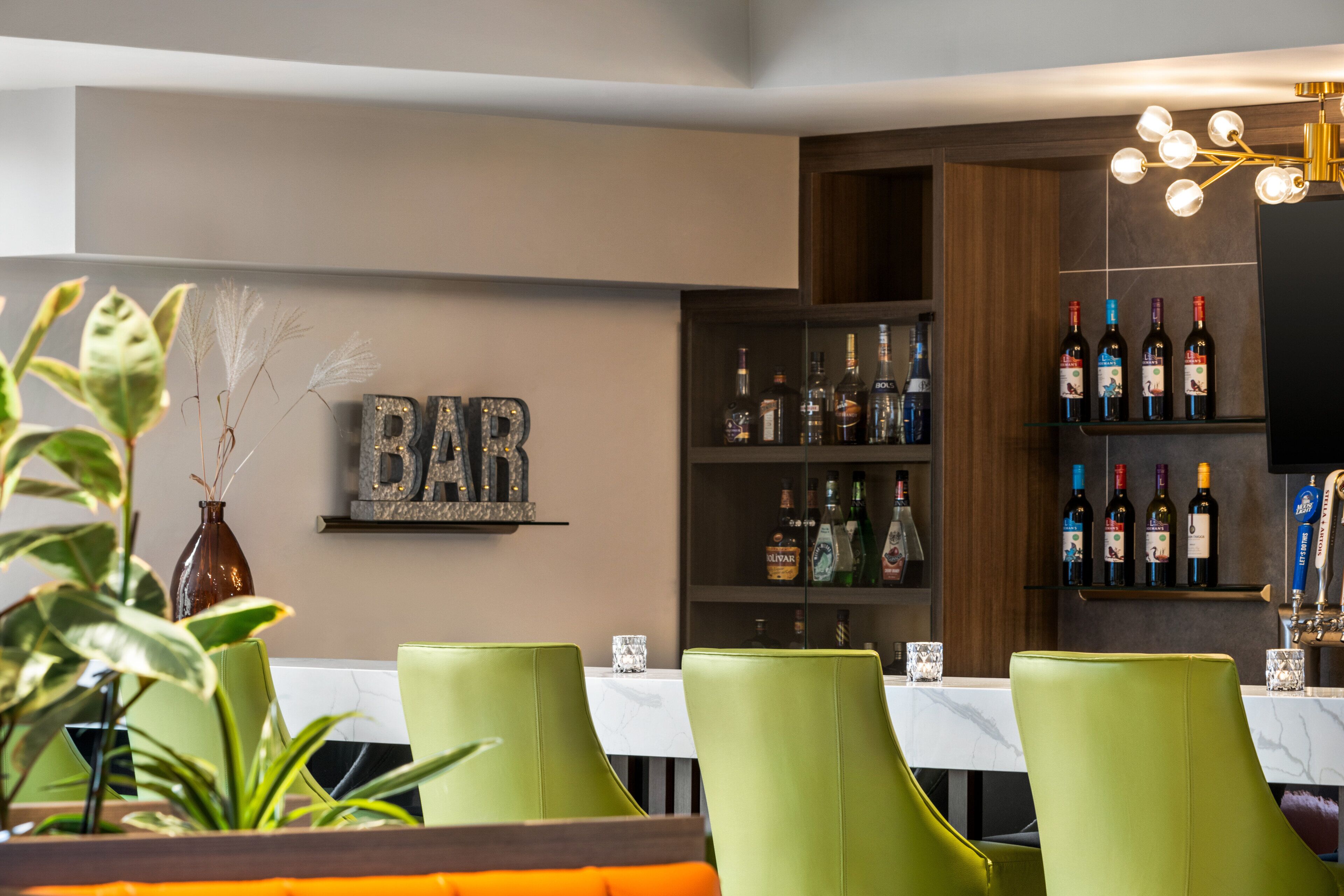 A bar area with green chairs, a shelf with liquor bottles, and a 'BAR' sign on the wall.