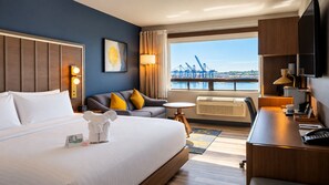 A hotel room with a bed, a sofa, a desk, a TV, and a window with a view of a bridge.