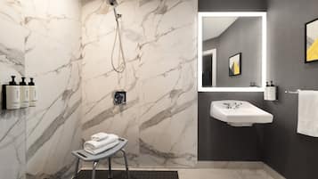 Un baño moderno con paredes de mármol, ducha, lavamanos y espejo.