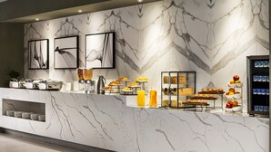 Una encimera de mármol con alimentos para el desayuno, obras de arte enmarcadas y un dispensador de bebidas.
