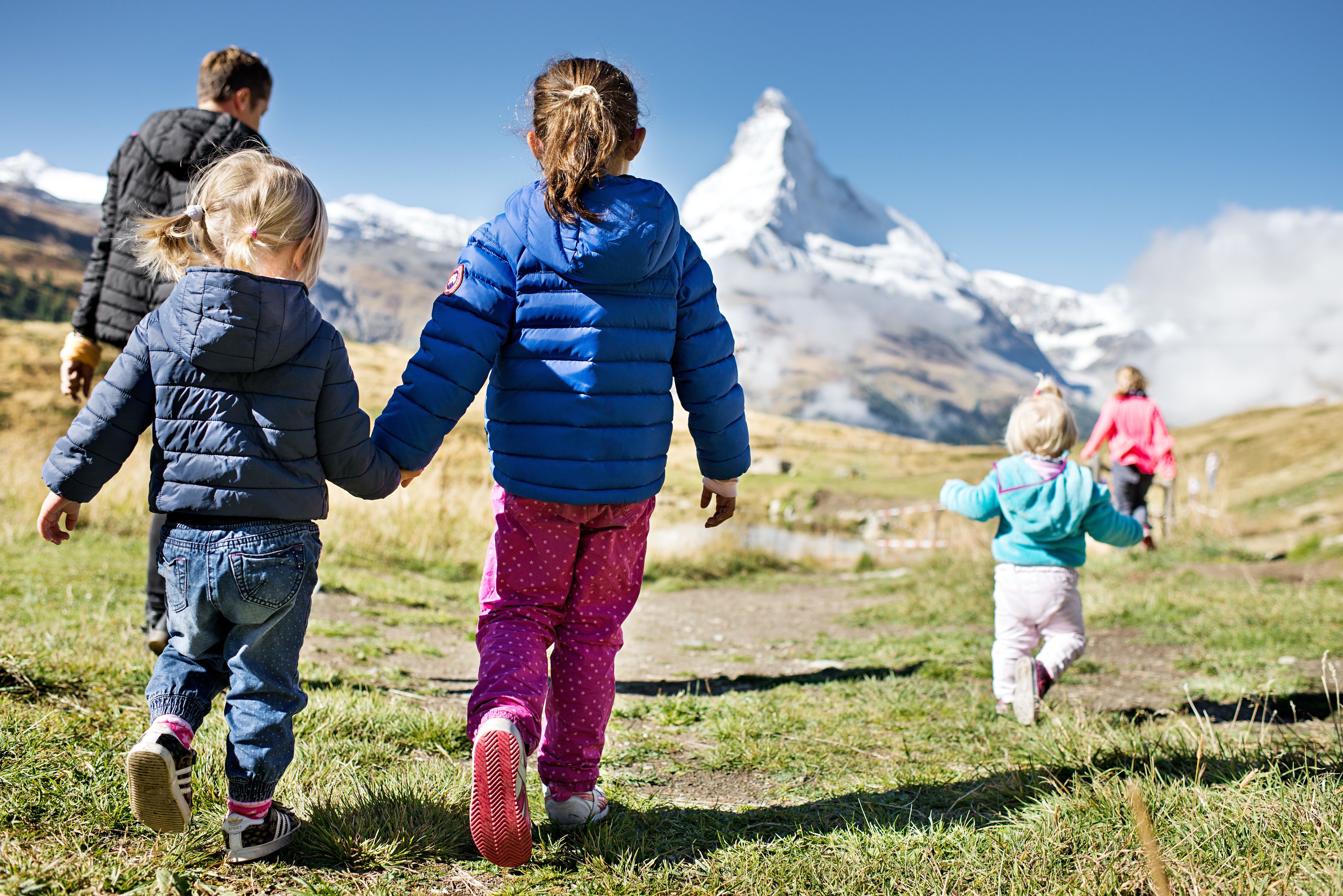 A group of people walking on a grassy path with a snow-capped mountain in the background.