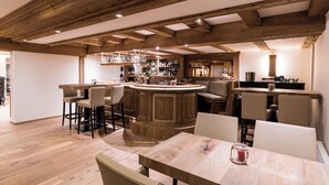 A spacious kitchen with wooden beams, a central island with bar stools, and a bar area with various bottles. - Hotel Butterfly (Zermatt)