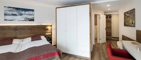 Un dormitorio con una cama, un armario, un banco rojo y un cuadro en la pared.