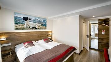 A hotel room with a bed, a wooden headboard, a painting of sheep on the wall, and a wooden wardrobe.