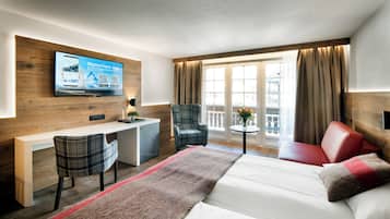 Ein Hotelzimmer mit einem Bett, einem Schreibtisch, zwei Stühlen, einem an der Wand befestigten Fernseher und einem Fenster mit Vorhängen.