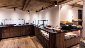 A breakfast bar with wooden cabinets, a variety of food items, and a rustic ceiling. - Hotel Butterfly (Zermatt)