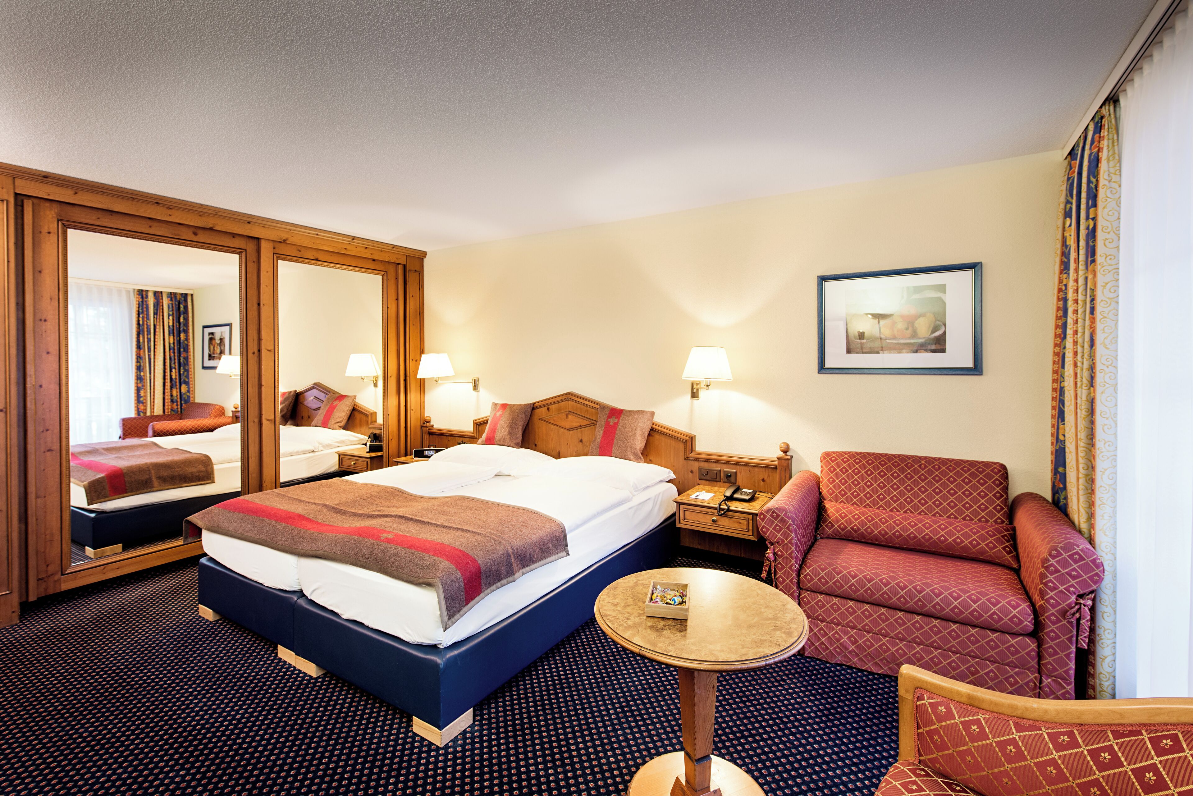 A hotel room with a large bed, two bedside tables, a chair, a round table, and a mirror.