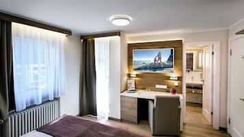 Une chambre d’hôtel équipée d’un lit, d’un bureau, d’une chaise, d’un téléviseur fixé au mur et d’une salle de bain visible à travers une porte ouverte.