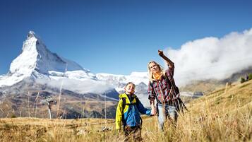 A person and a child in a grassy field with a mountain in the background.