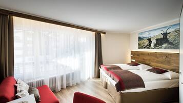 A hotel room with a bed, a red sofa, and a painting of goats on the wall.