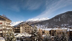 A hotel with multiple floors, a ski resort in the background, and snow-covered trees. - Hotel Butterfly (Zermatt)