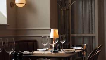 Una mesa de comedor dispuesta con copas de vino, platos y cubiertos, con una lámpara y un juego de salero y pimentero encima.