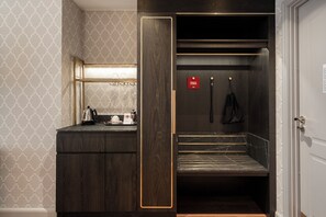 Habitación de hotel con tocador de madera oscura, un espejo, una mesita con tetera y tazas, y un cartel rojo en la puerta.