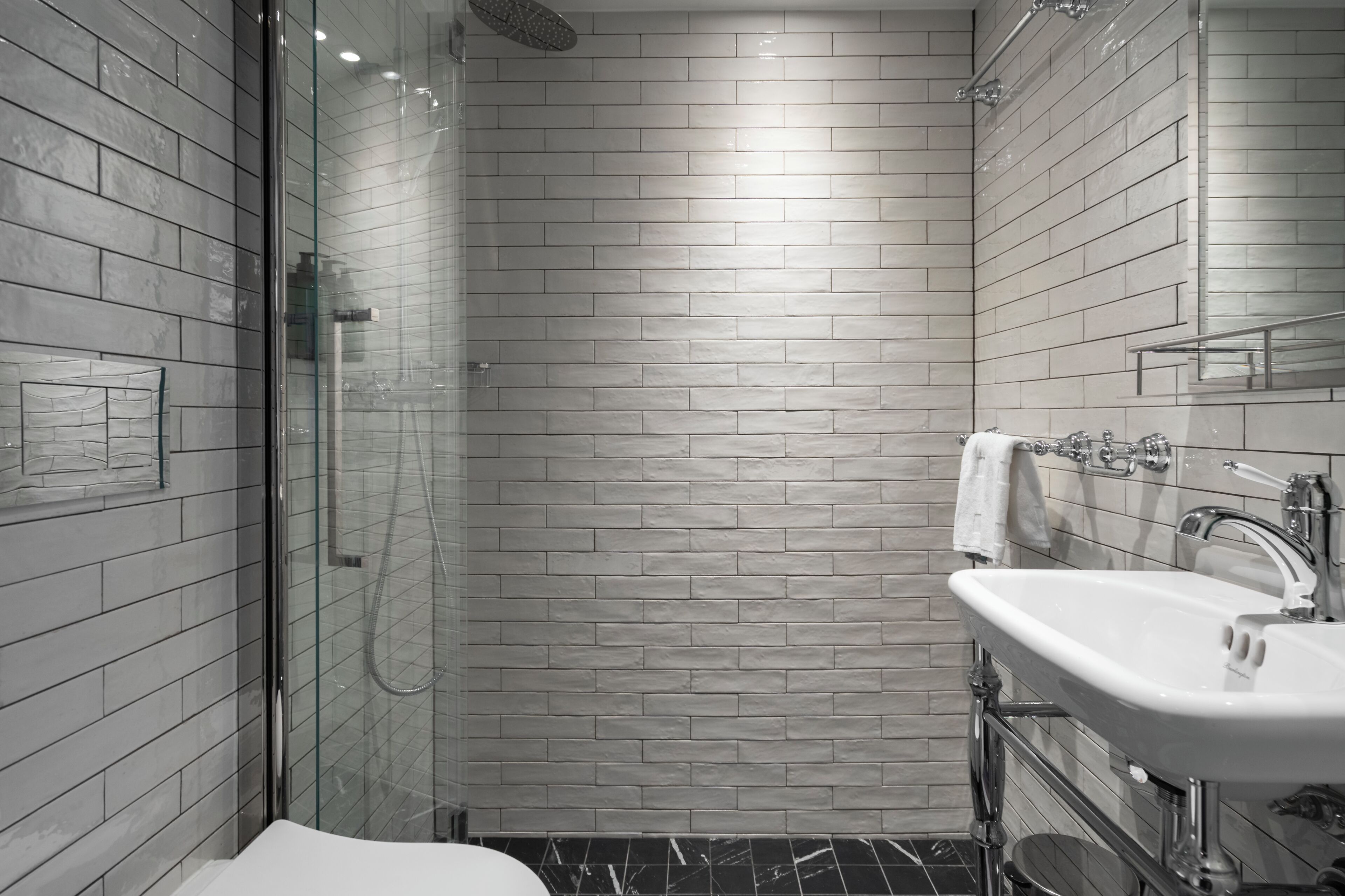 Un bagno moderno con doccia vetrata, lavandino bianco e pavimento piastrellato.