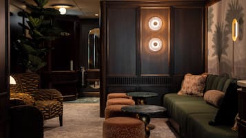 A dimly lit lounge area with a sofa, ottomans, a round table, and a large plant.