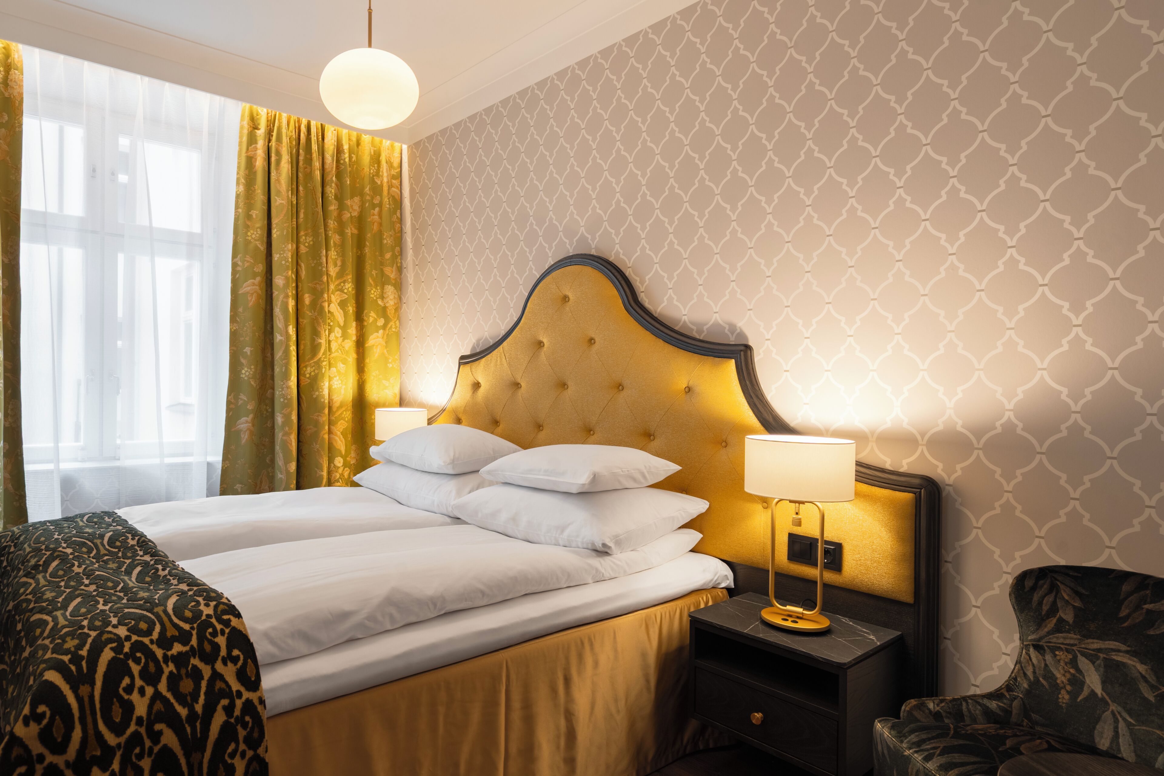 A hotel room with a bed, a nightstand, a lamp, a chair, and a window with curtains.