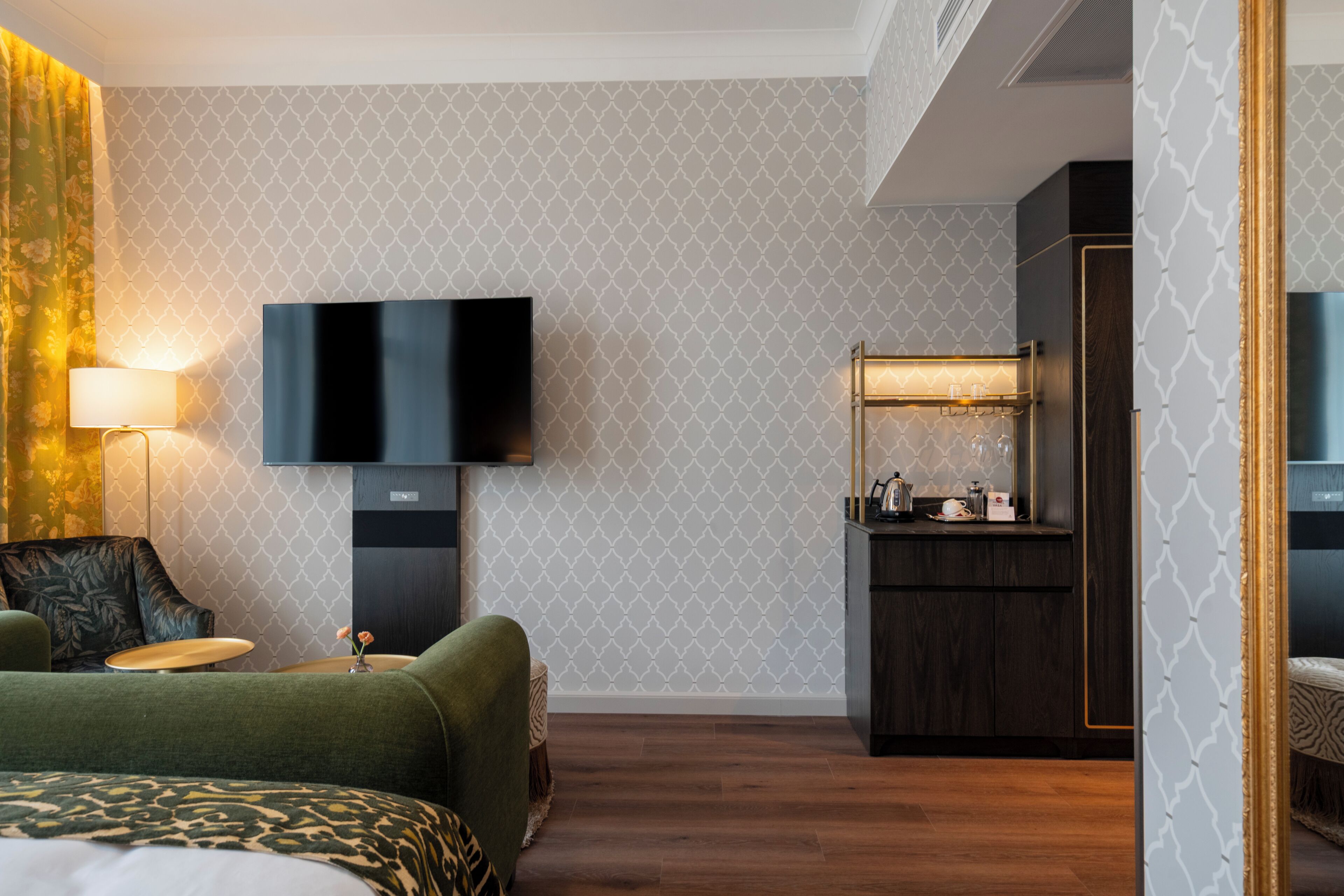 A hotel room with a bed, a TV, a desk, and a small kitchenette.