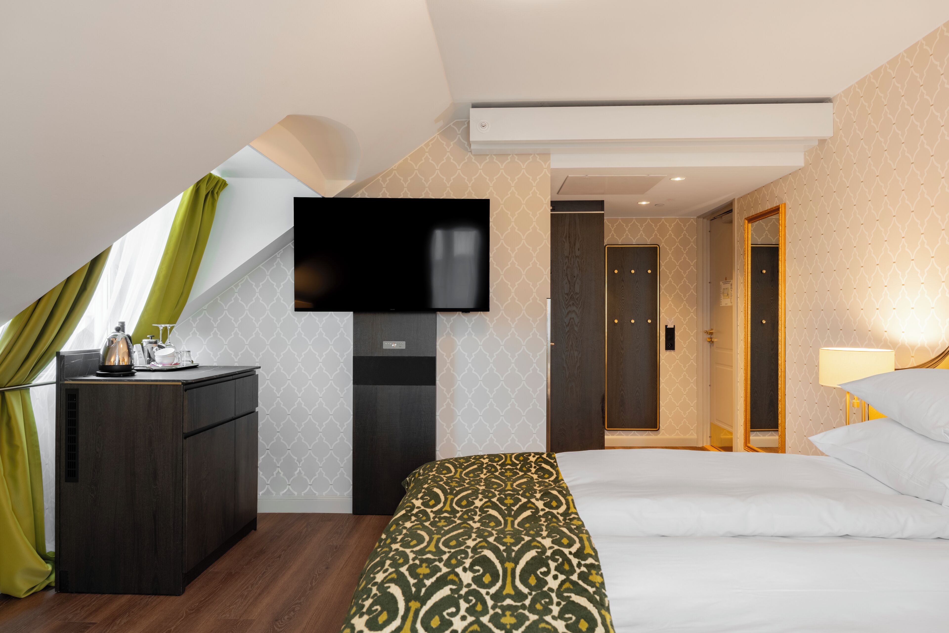 A modern hotel room with a bed, a desk, a flat-screen TV, and a walk-in closet.