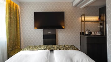 Habitación de hotel con cama, televisor montado en la pared, una pequeña mesa de escritorio con espejo y ventana con cortinas.