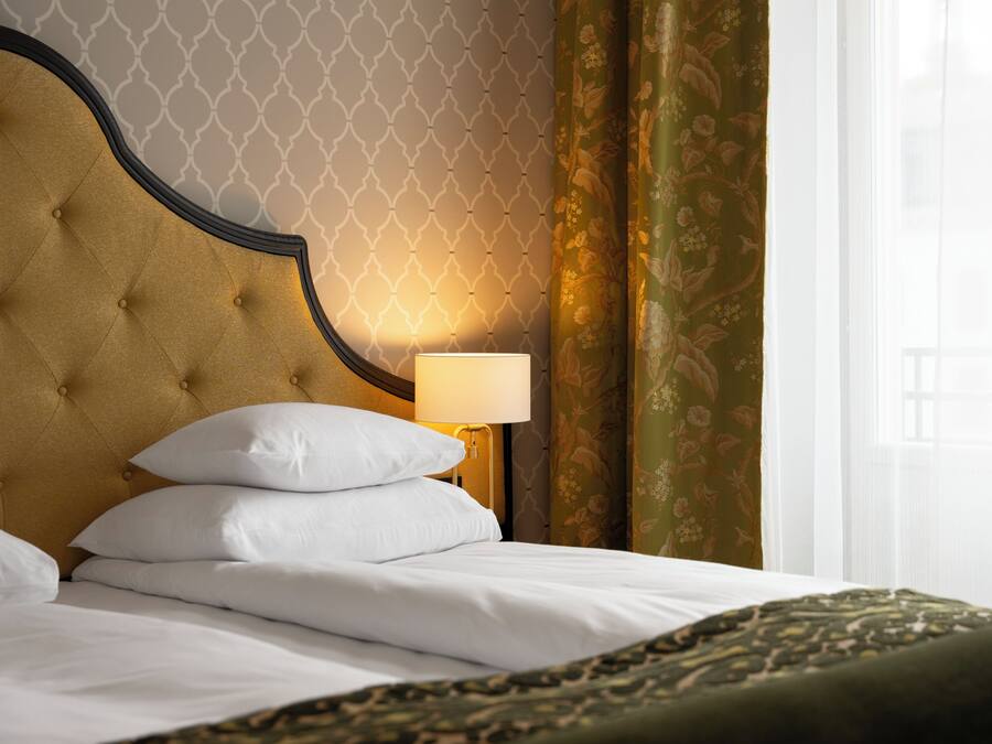 Una cama bien hecha con sábanas y almohadas blancas, un cabecero capitonado y una lámpara de noche.
