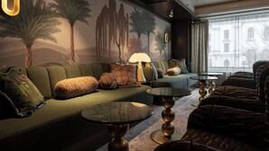 Un salón moderno con un sofá verde, mesas redondas y un mural de árboles.