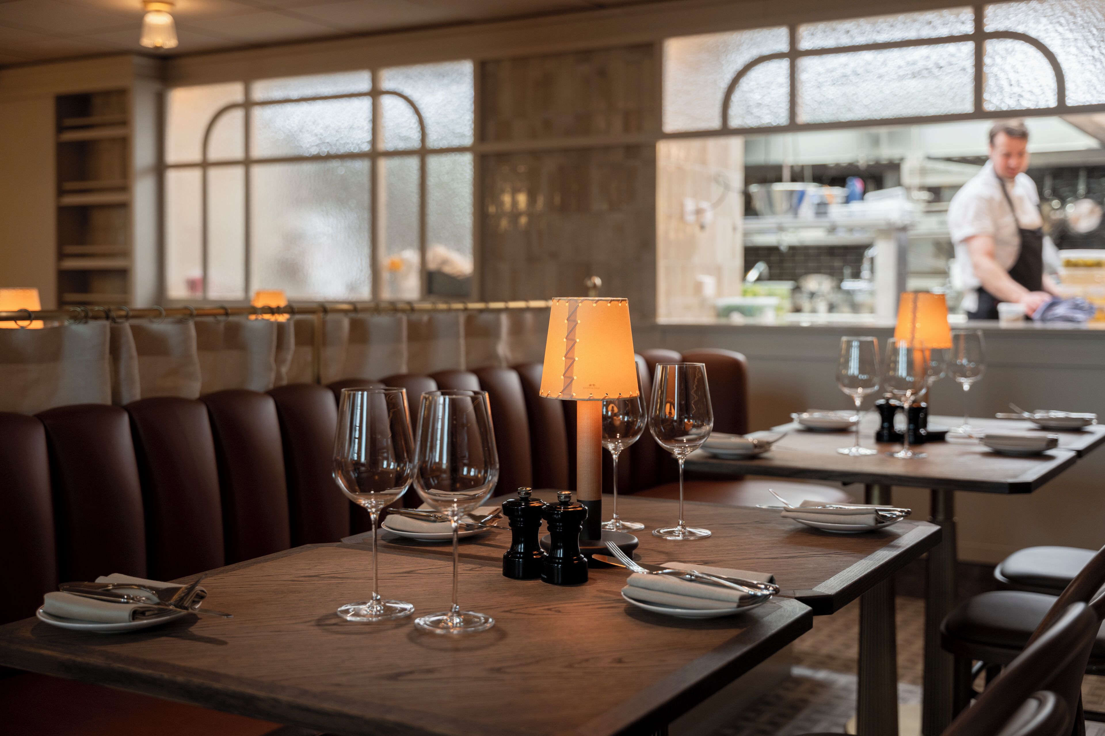 Interior de restaurante con mesas de madera listas para comer, una zona de bar y vistas a través de la ventana.