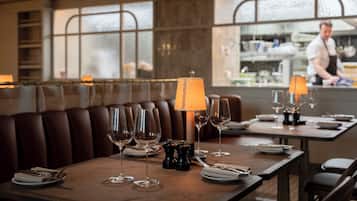 Interior de restaurante con mesas de madera listas para comer, una zona de bar y vistas a través de la ventana.