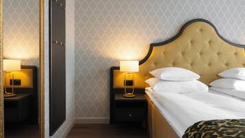 A hotel room with a bed, nightstands, a mirror, and a patterned wallpaper.