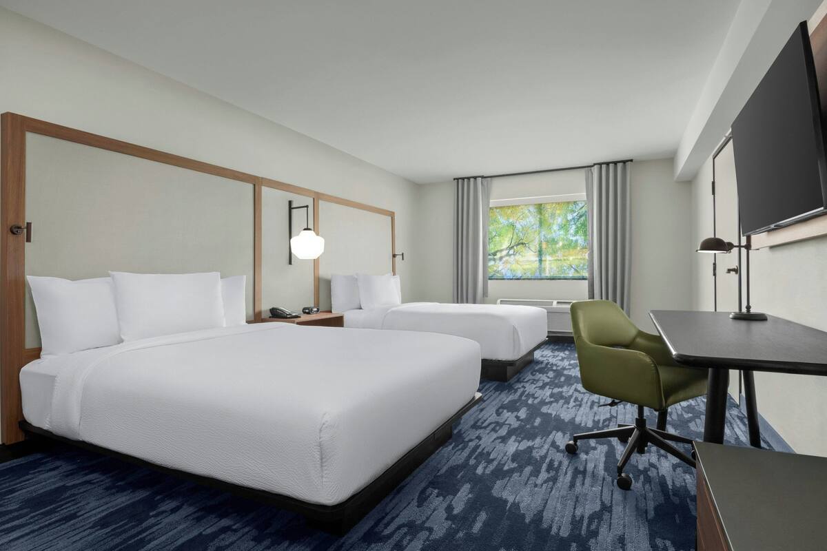 Une chambre d’hôtel avec deux lits, un bureau, une chaise, une télévision et une fenêtre avec des rideaux.