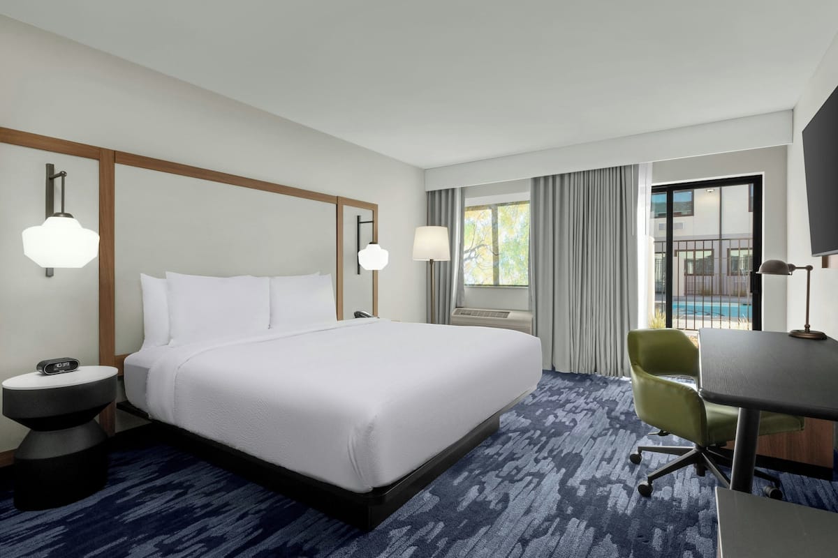 Une chambre d’hôtel avec un grand lit, un bureau, une chaise, une télévision et une fenêtre avec des rideaux.