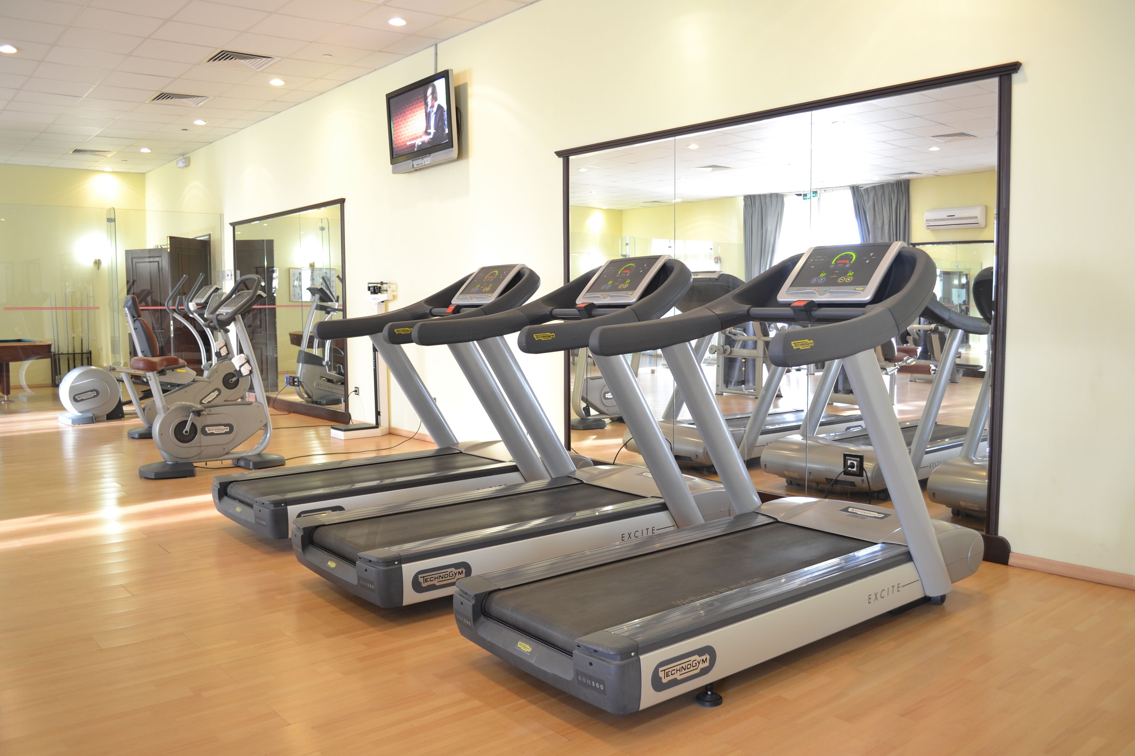 Un gimnasio con cintas de correr, bicicletas estáticas y espejos.