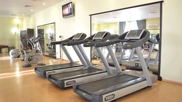 Un gimnasio con cintas de correr, bicicletas estáticas y espejos.
