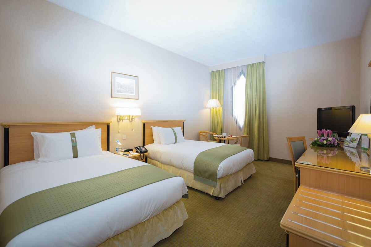 Une chambre d’hôtel avec deux lits, un bureau, une télévision et une fenêtre avec des rideaux.