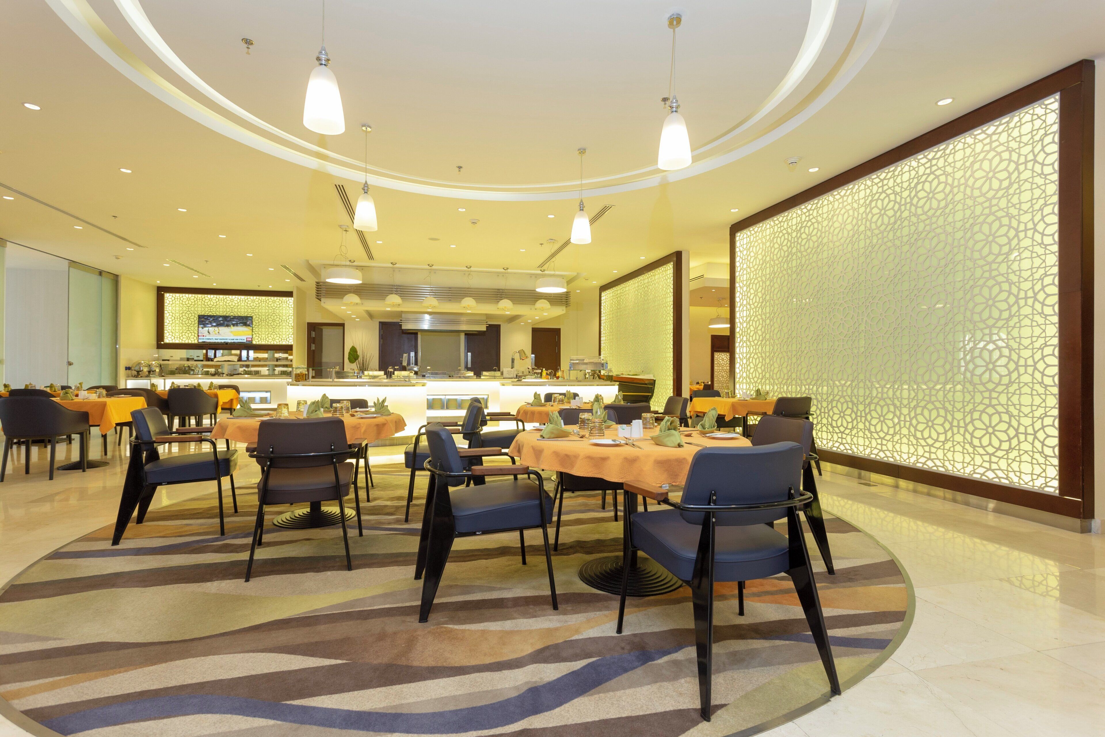 A hotel dining area with round tables, chairs, and a central kitchen.