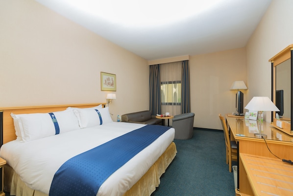 A hotel room with a large bed, a desk, a chair, a small table, and a window with curtains.