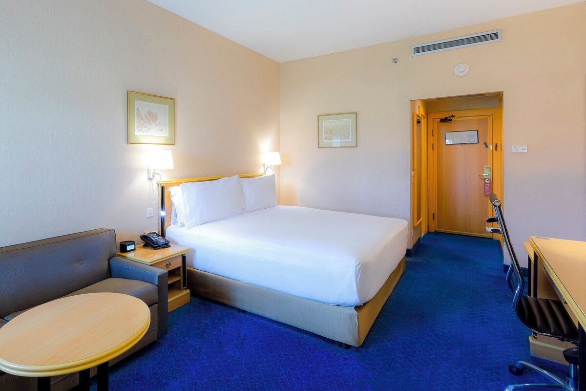 Une chambre d’hôtel avec un lit, un petit canapé, une table ronde et un bureau avec une lampe.