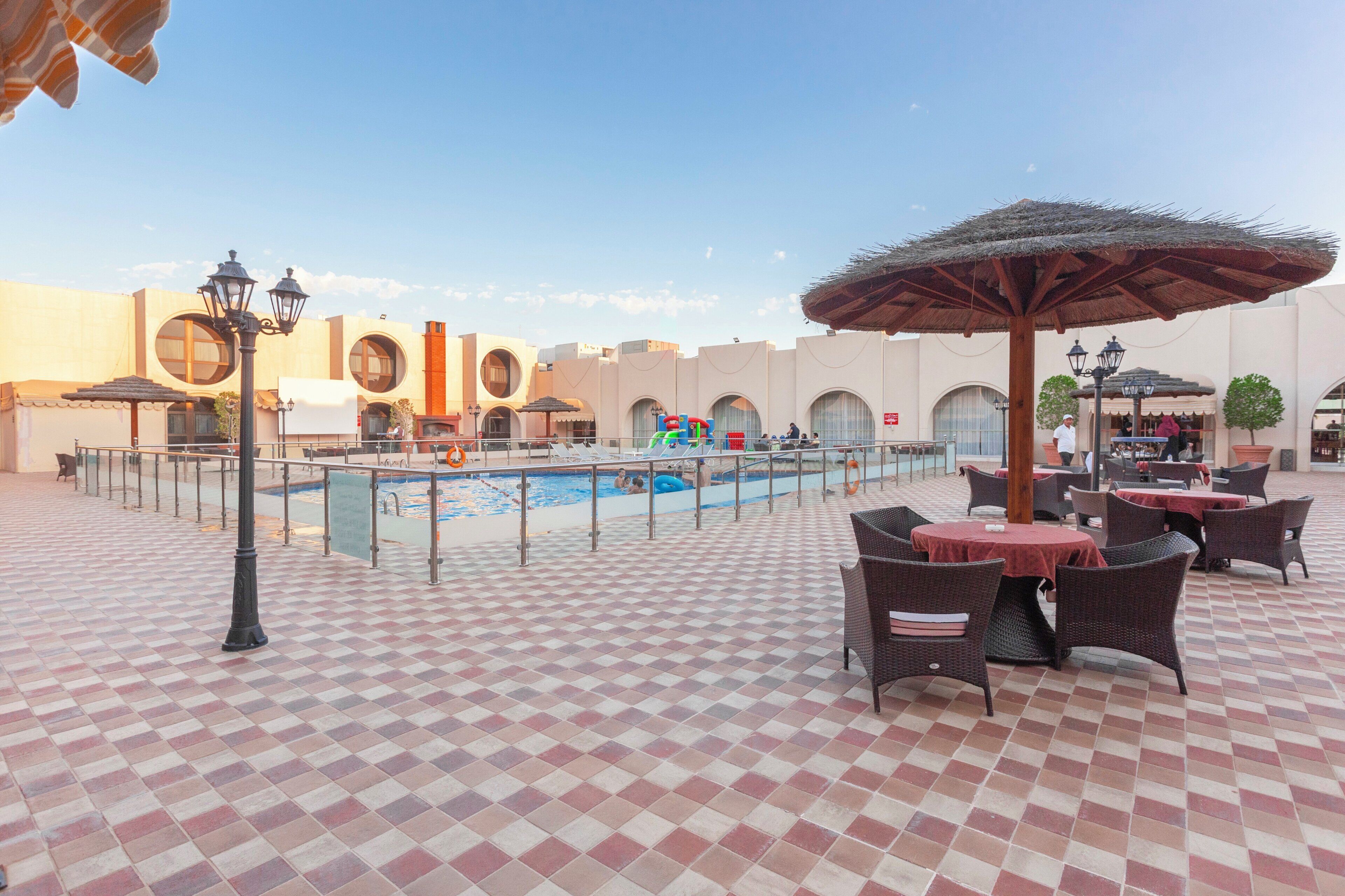 A poolside area with a checkered floor, lounge chairs, and umbrellas.