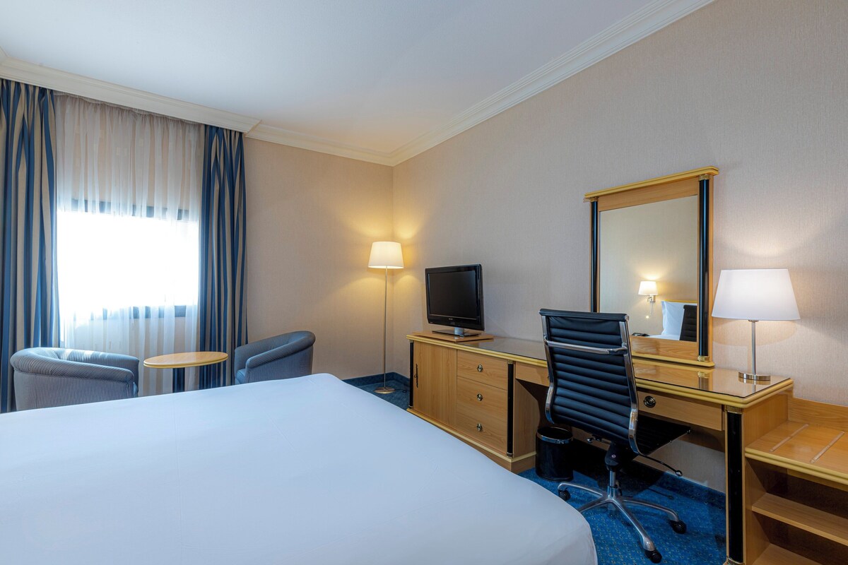 Une chambre d’hôtel comprenant un lit, un bureau avec un ordinateur, une chaise, une télévision et un miroir.