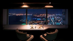 Comedor con vista panorámica nocturna de la ciudad, con una mesa, platos, cubiertos y dos sillas.