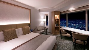 Una habitación de hotel con una cama grande, un escritorio y vistas a un paisaje urbano de noche.