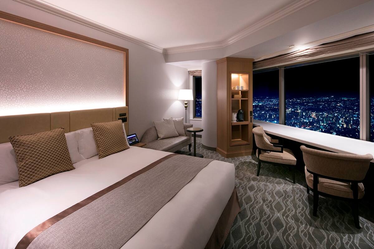 A hotel room with a large bed, a desk, and a view of a cityscape at night.