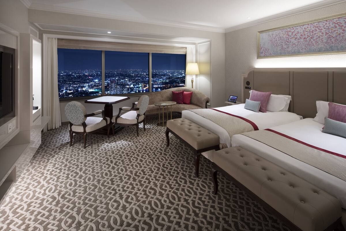 A hotel room with a city view, a large bed, a sofa, a dining table, and a TV.